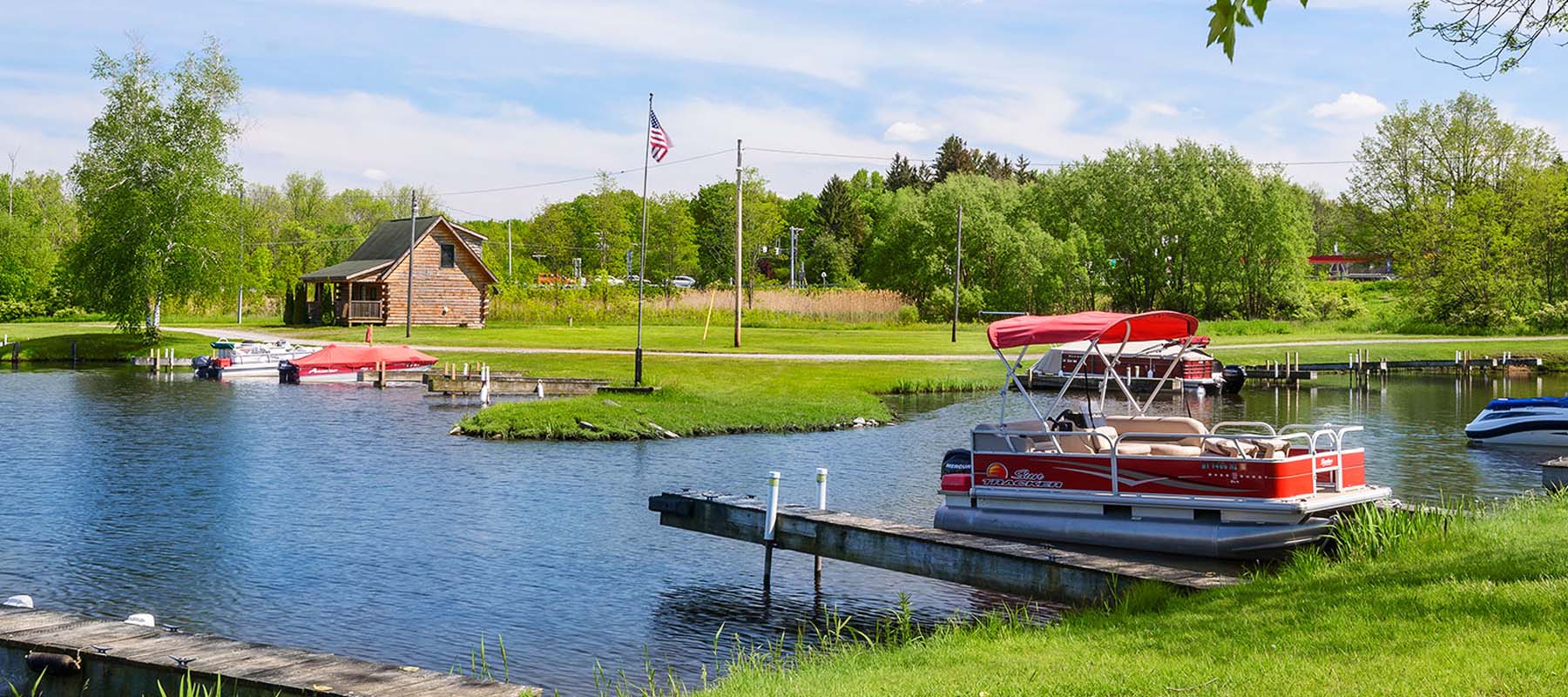 pontoon boat docked on a marina with green grass and cabin in the distance