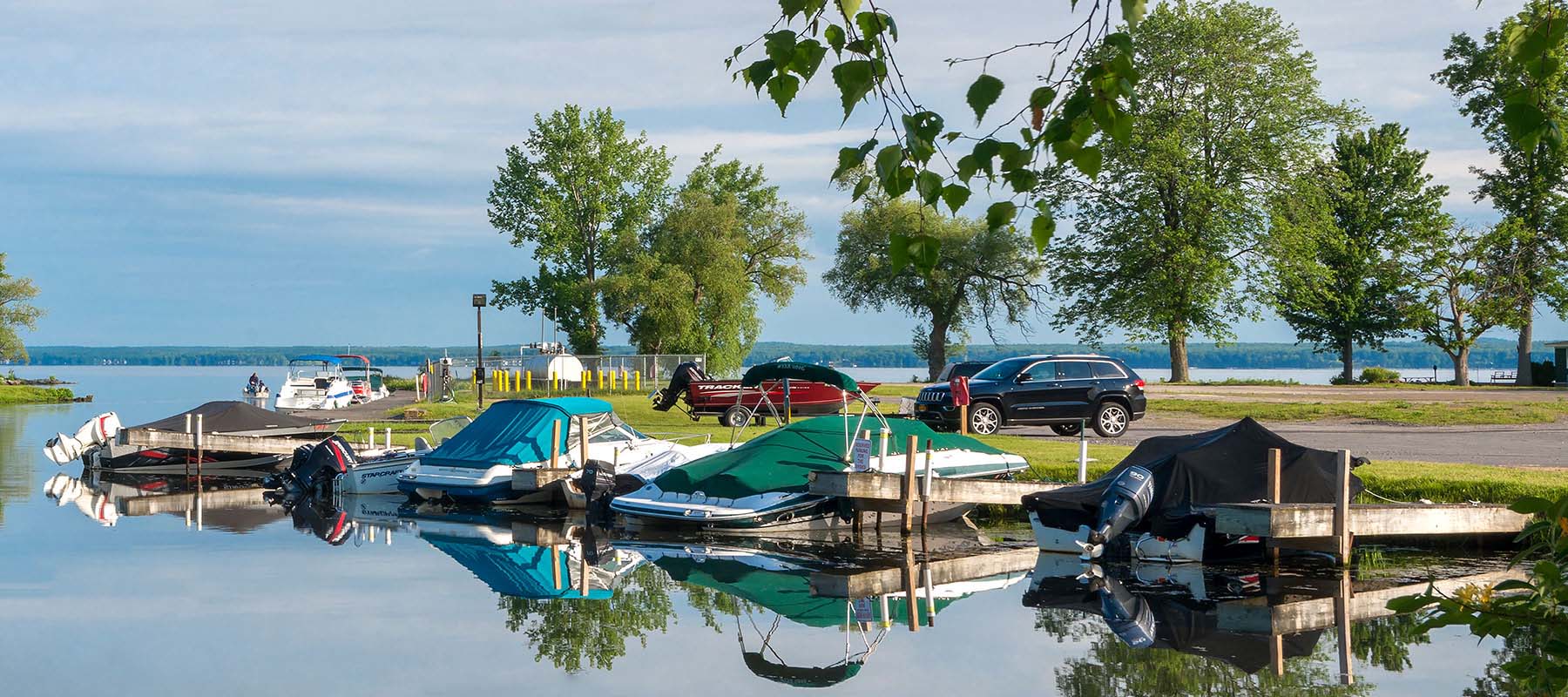 covered boats docked at marina with cars in the parking lot in the distance